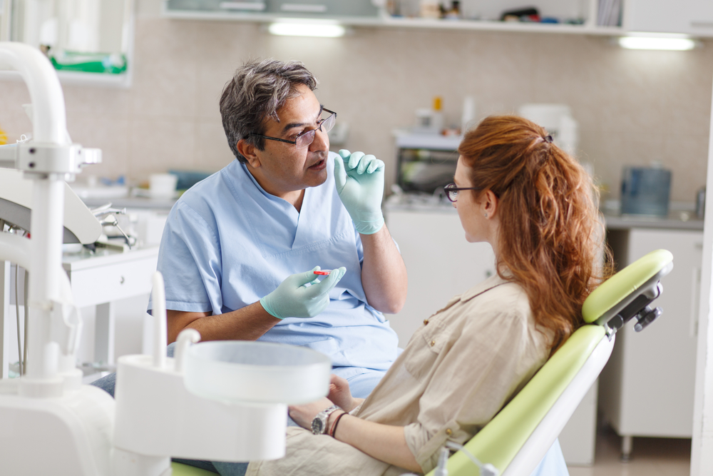 patient with red hair sitting in dental chair listening to dentist speak